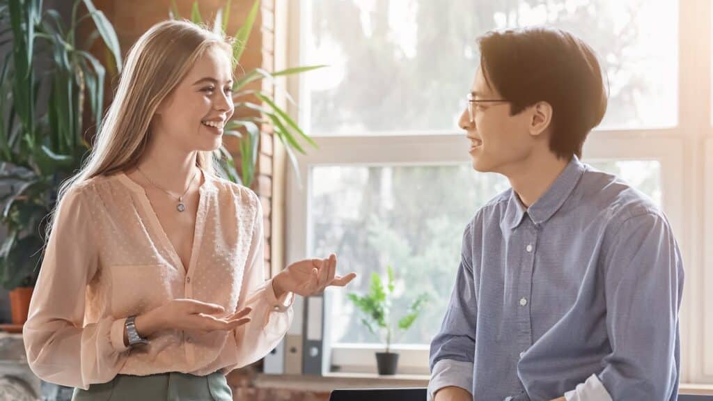 Asian man and caucasian woman having conversation at workplace, office flirting